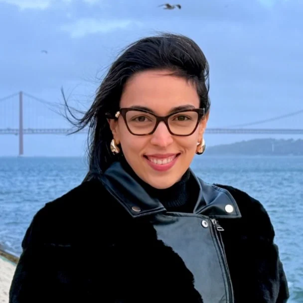 Sara Medeiros de óculos, ao ar livre, com uma ponte ao fundo.